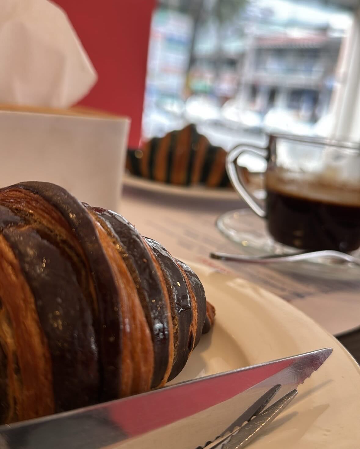 A flaky croissant on a plate beside a cup of coffee at Belle Lyipa.