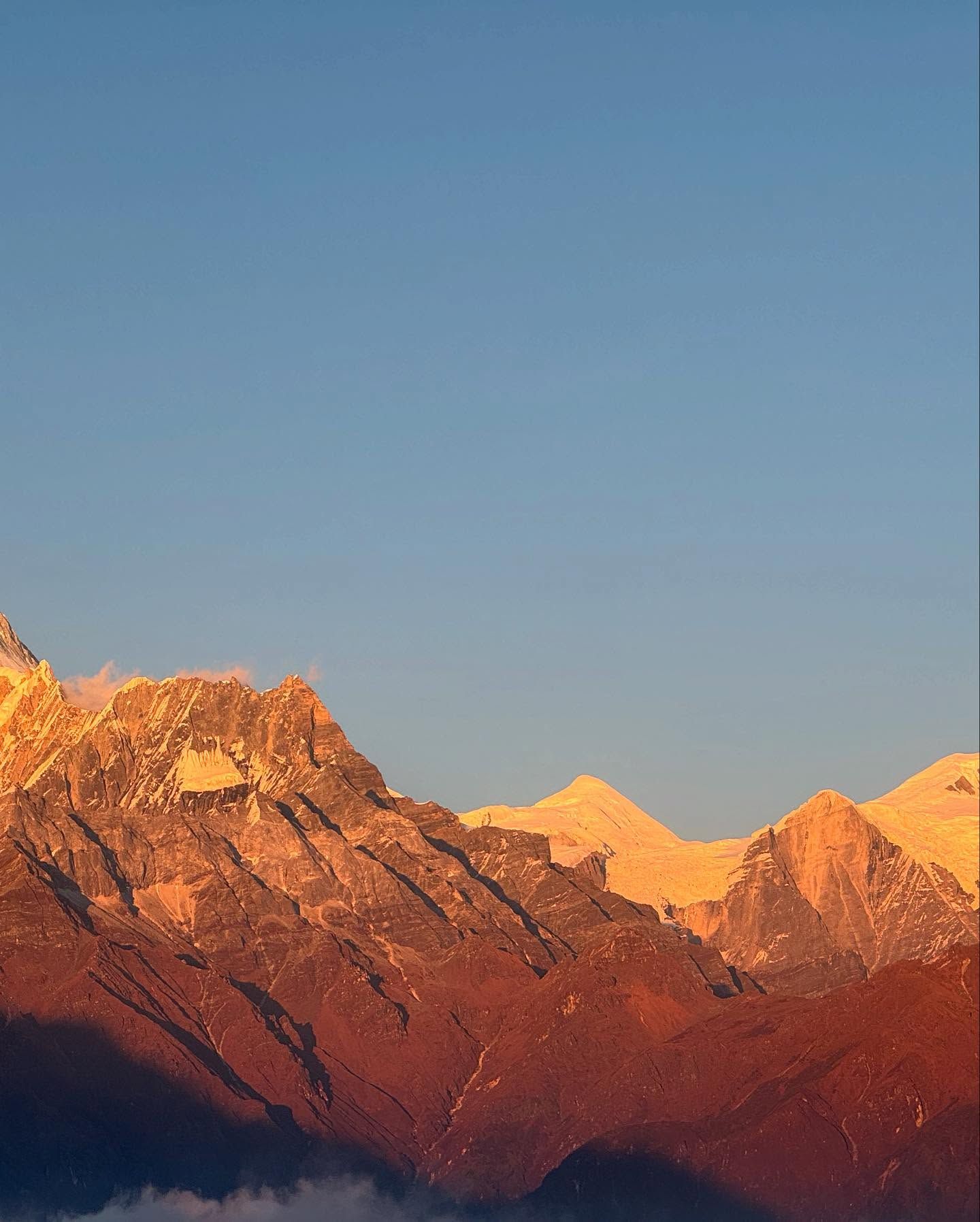 A row of rocky peaks glowing deep red and orange at sunset, under a clear sky.